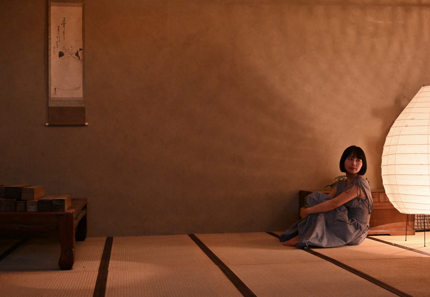 畳の部屋の窓辺に座る人物と丸い照明